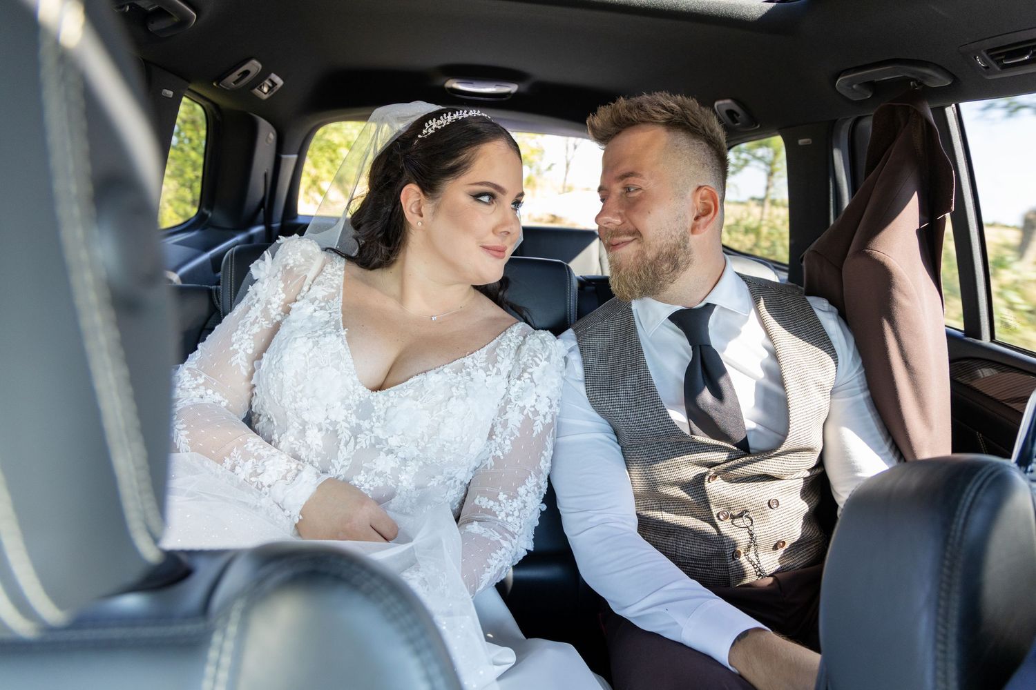 Candid moment captured of couple in wedding attire inside car.