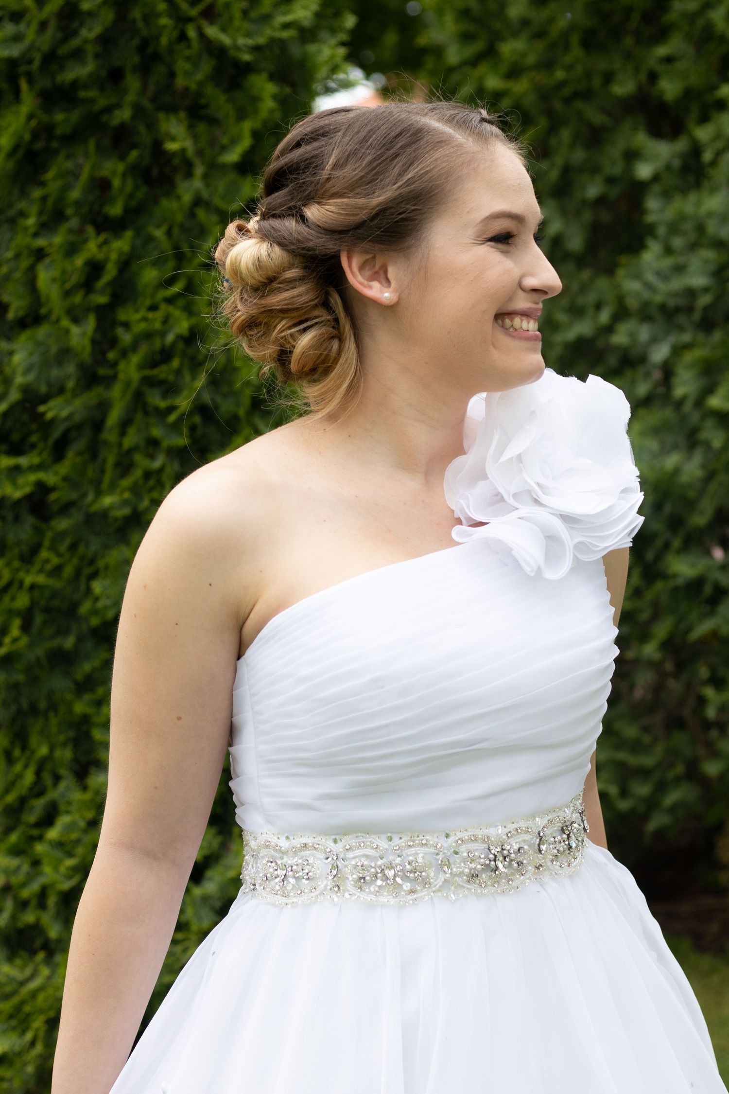 A one-shoulder white wedding gown features an elegant crystal belt detail.