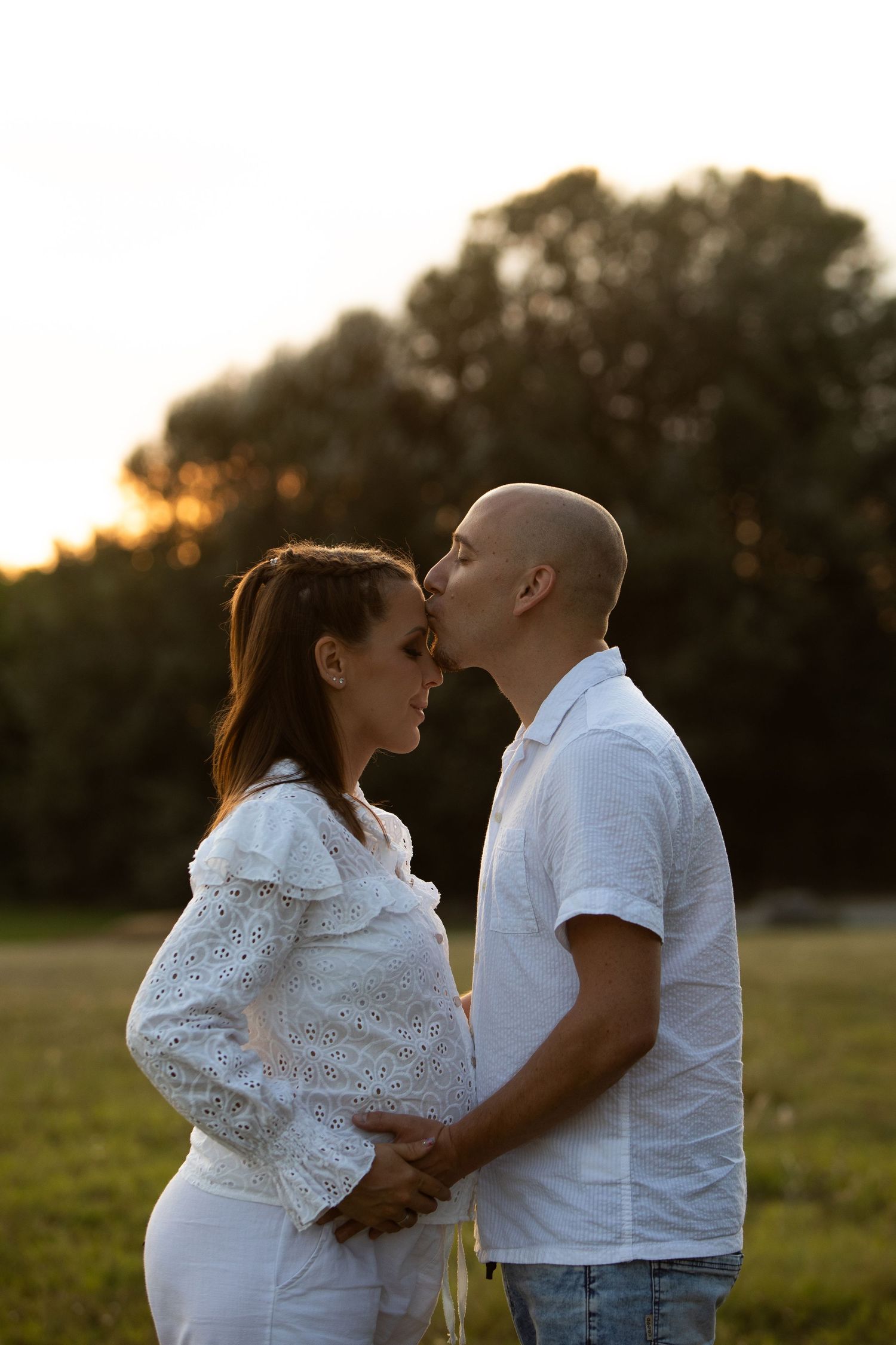 A couple in white outfits shares tender moments during golden hour.