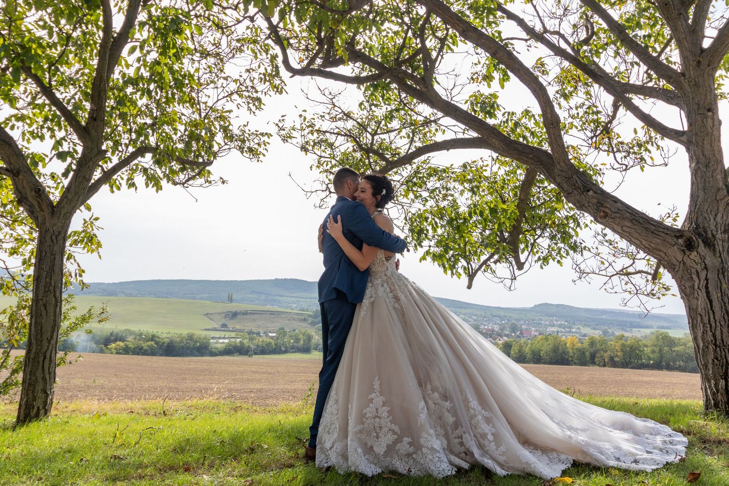 A romantic wedding portrait under blooming trees with rolling hills in the background.