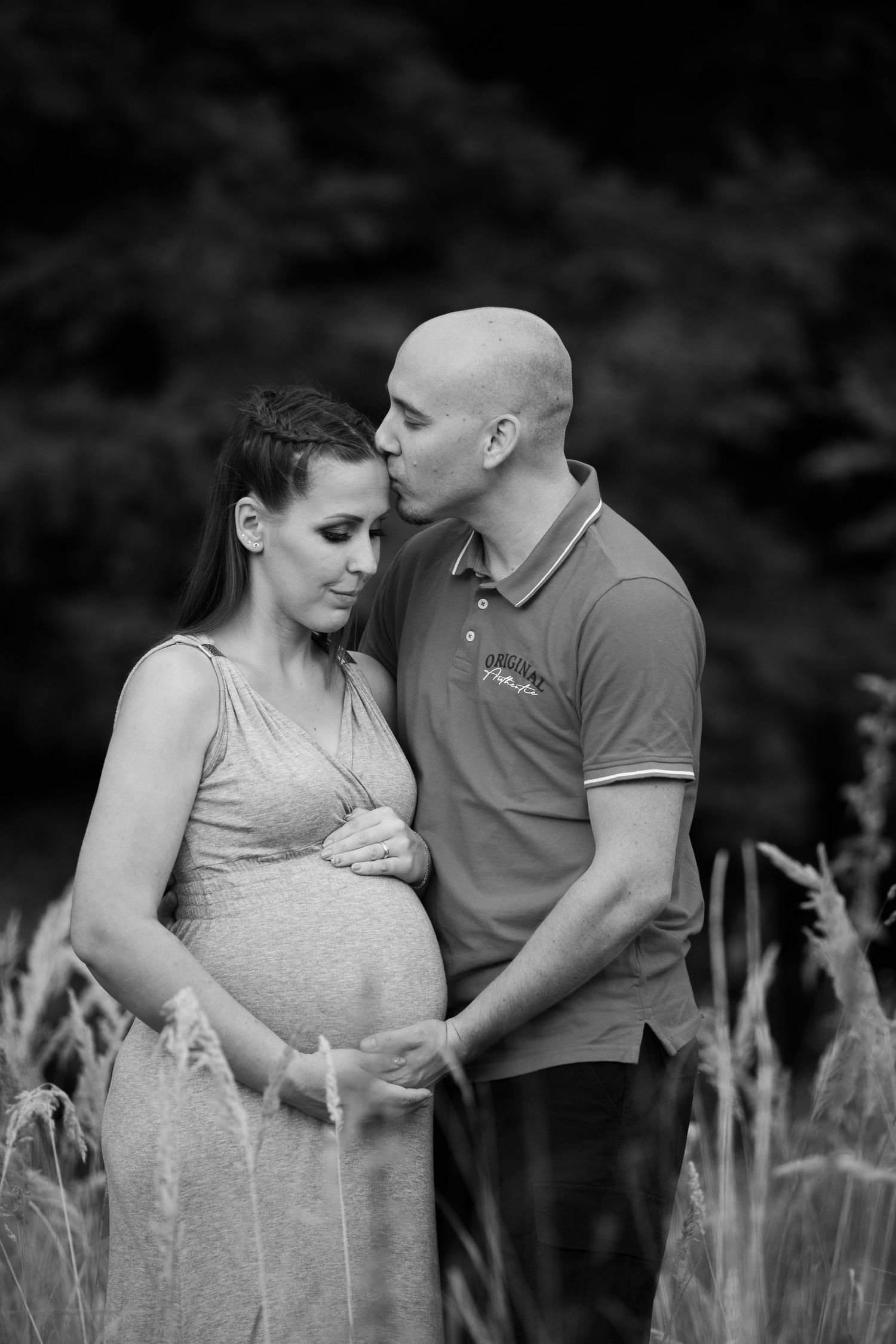 Black and white maternity photos showing tender moments between expecting couple in a natural setting.