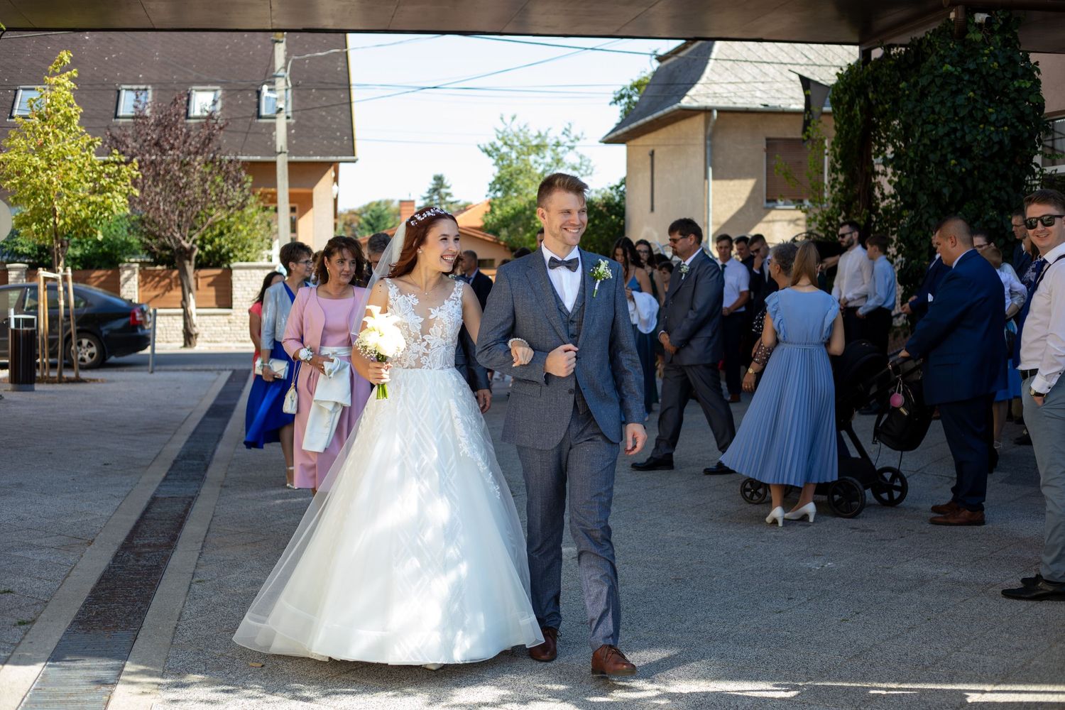 Wedding party processional walking down sunny street with bride in white gown.