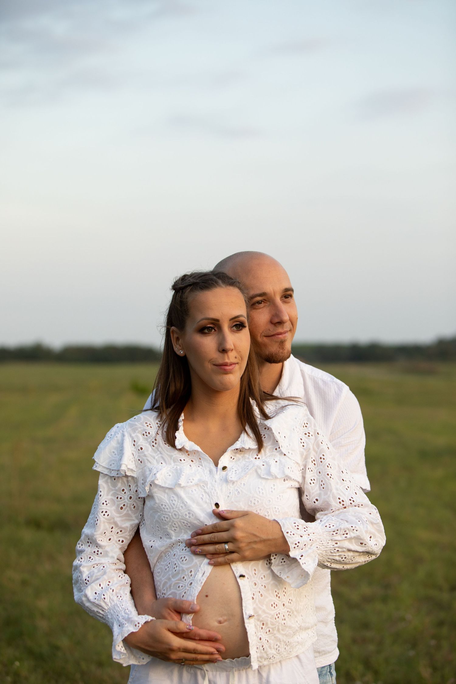 A couple in white clothing embraces in a sunlit field.