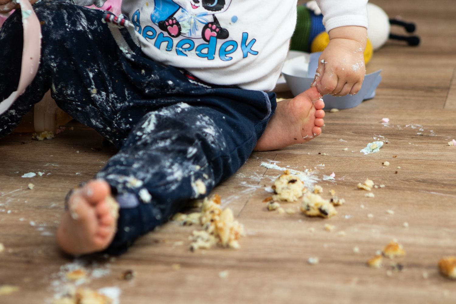 Messy cake crumbs scattered on wooden floor after cake smash photo session.