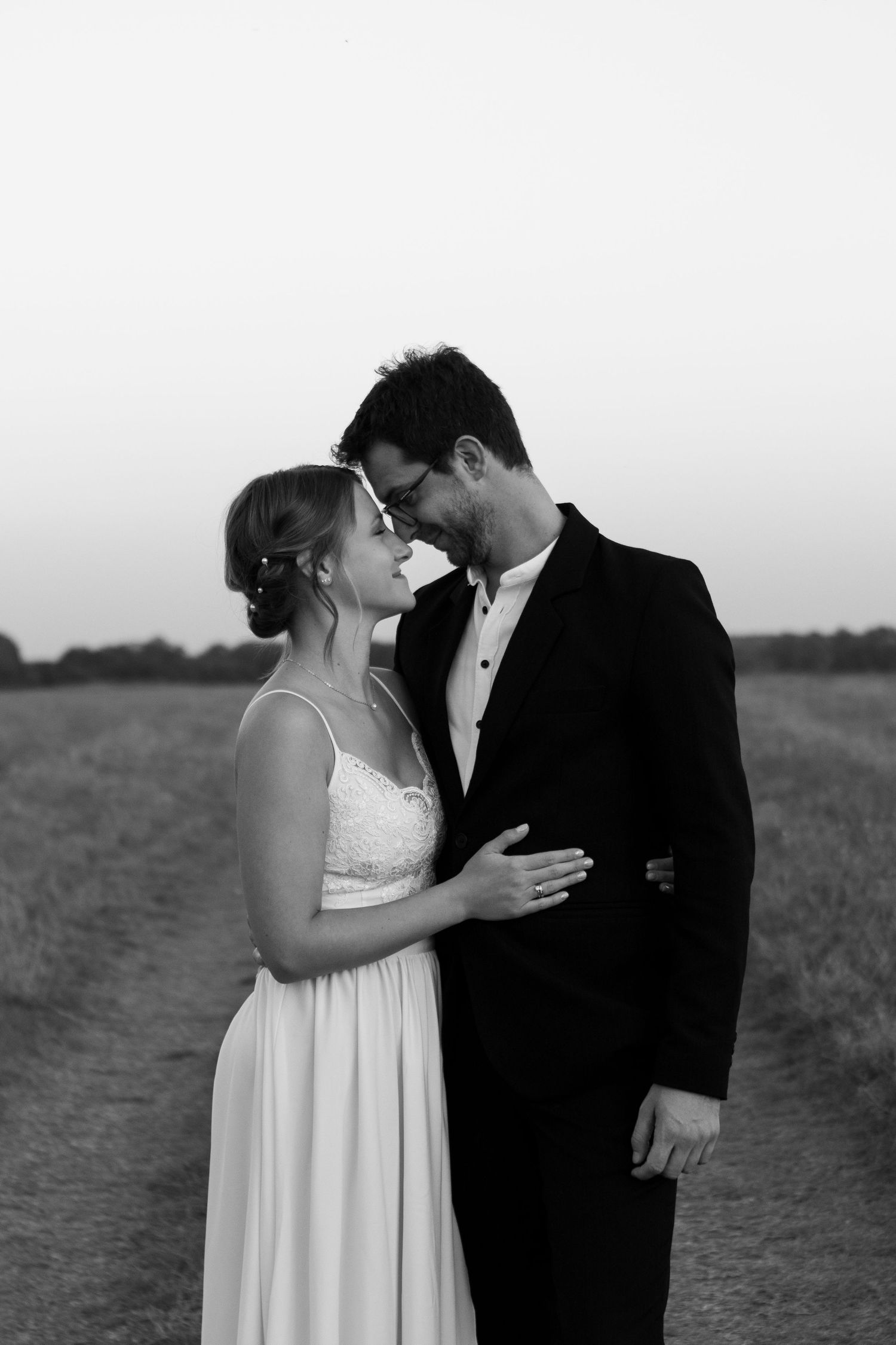 Black and white portrait of a romantic wedding couple embracing in a field.