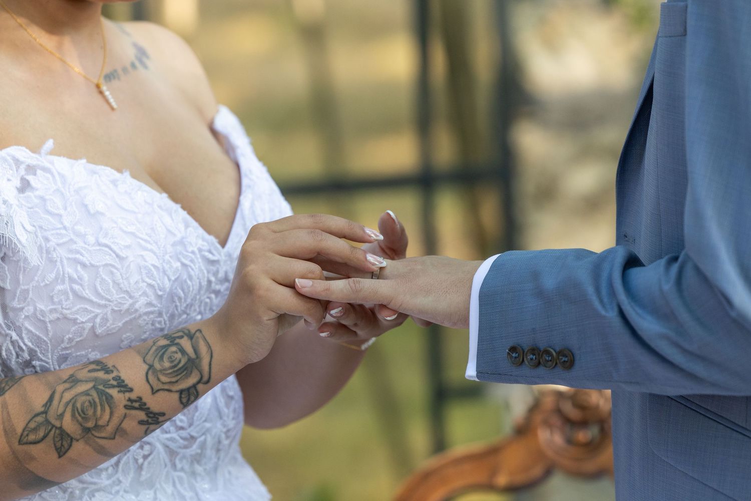 Close-up of hands exchanging wedding rings during ceremony, with bride's floral tattoo visible on arm.