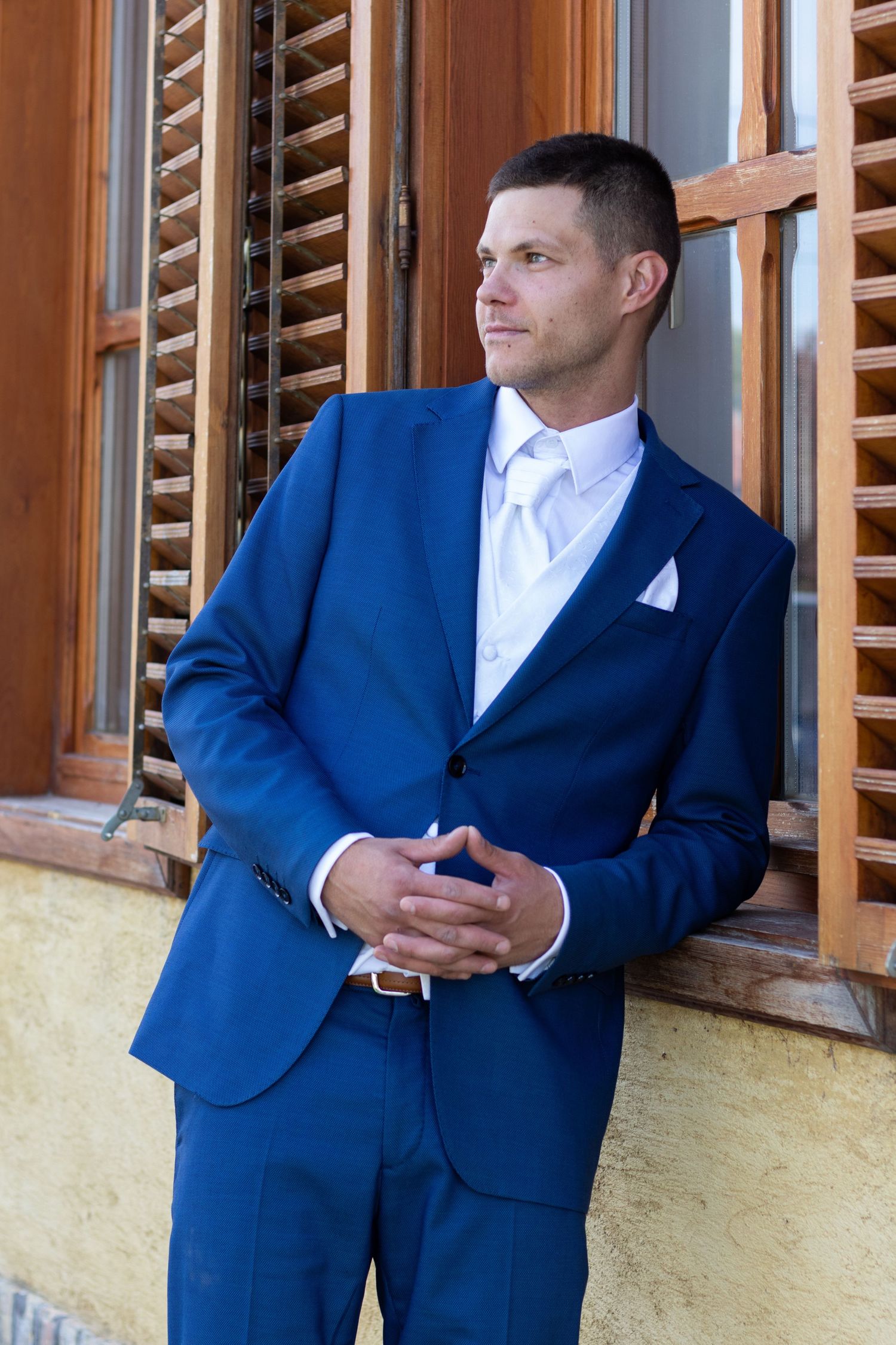 A formal portrait shows a well-dressed person in a navy blue suit and white tie looking to the side.