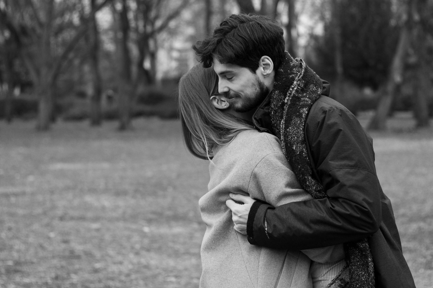 A couple embracing in a park during autumn with bare trees in the background.