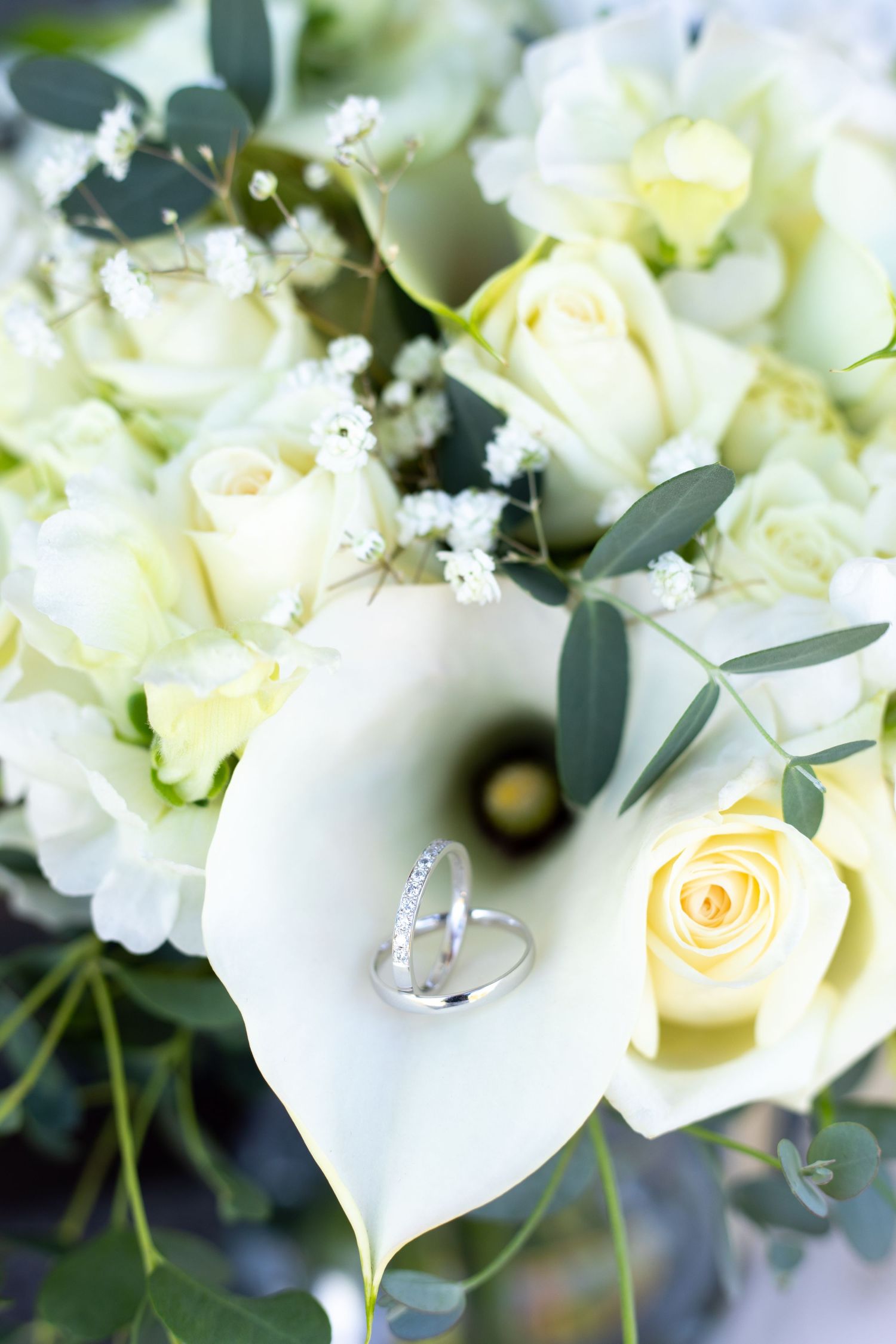 Elegant white roses and calla lilies in a wedding bouquet with diamond ring detail.