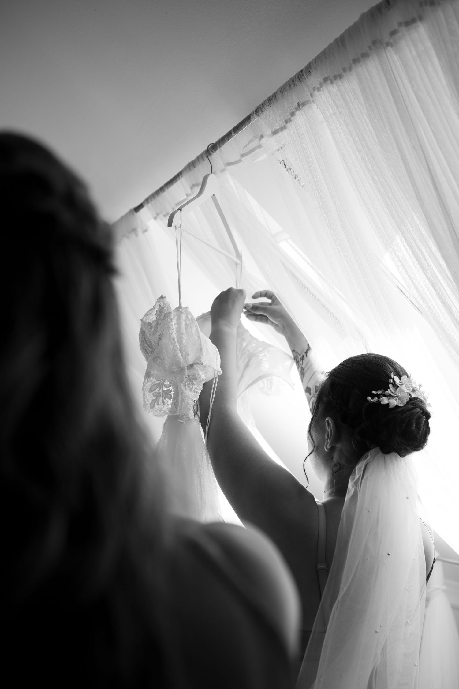 Black and white image of wedding dress preparations with flowing white fabric and natural light.
