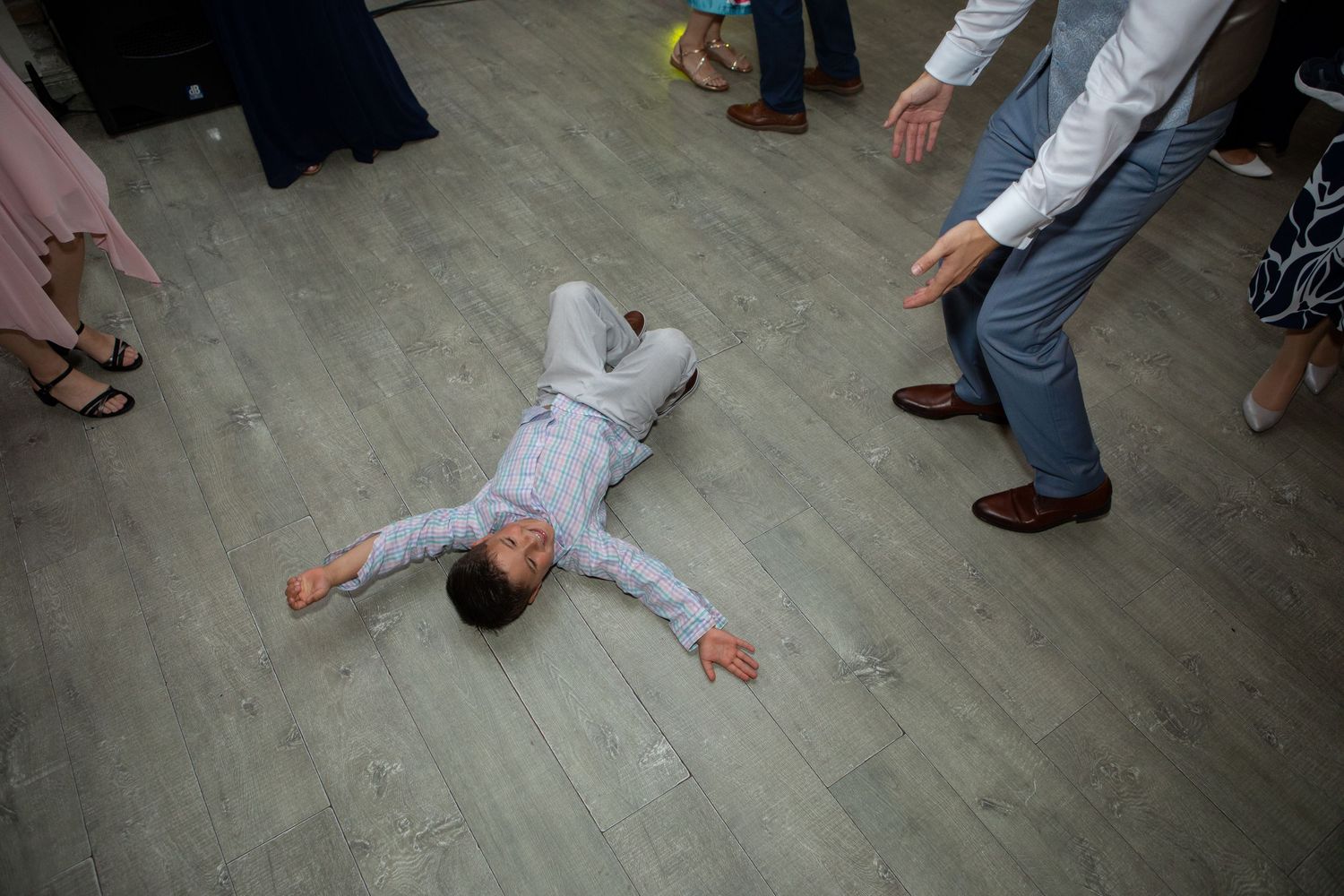 Young child in formal attire lies spread-eagled on dance floor during wedding reception.