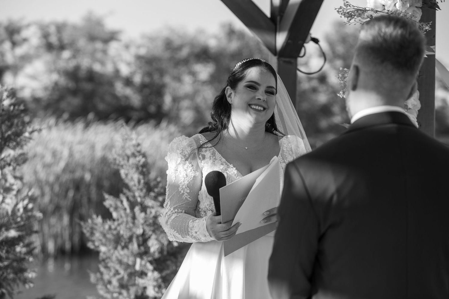 A couple exchanges wedding vows during an outdoor ceremony with lush greenery in the background.