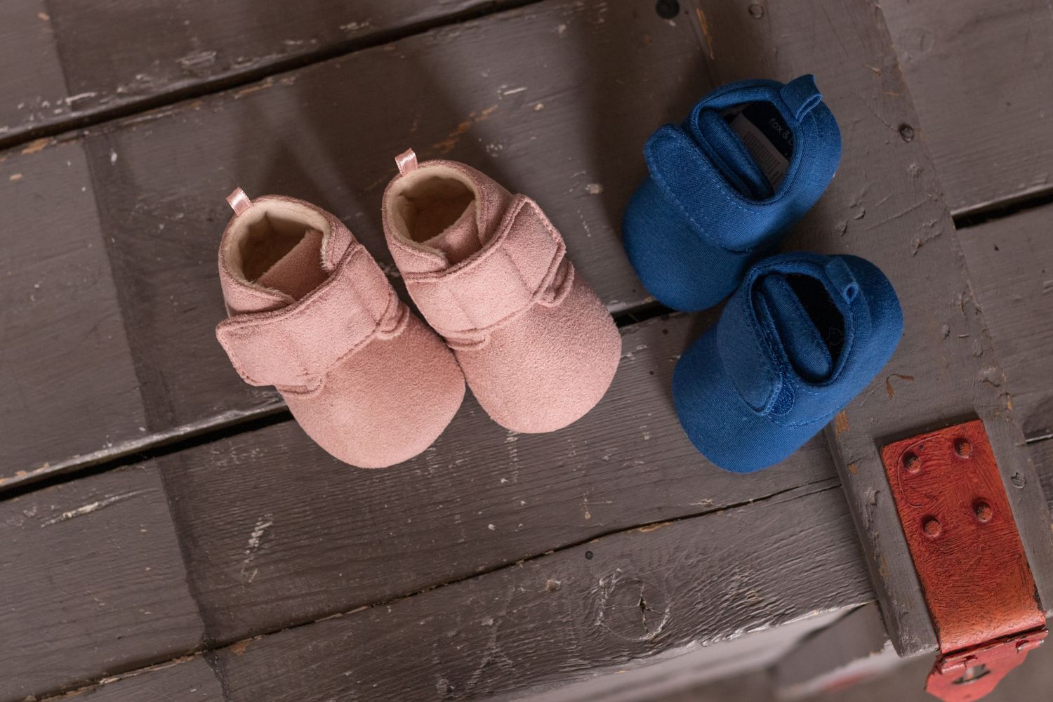 Pink and blue baby shoes arranged on dark wooden surface.