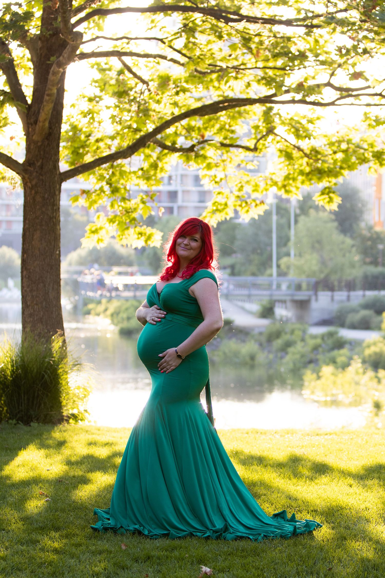 Maternity photos in emerald green dress by river during golden hour.