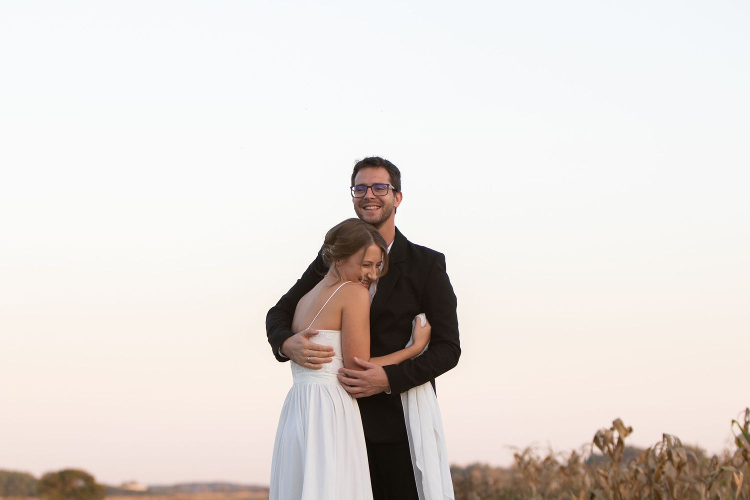 Newlywed couple dancing together in an outdoor field during golden hour.