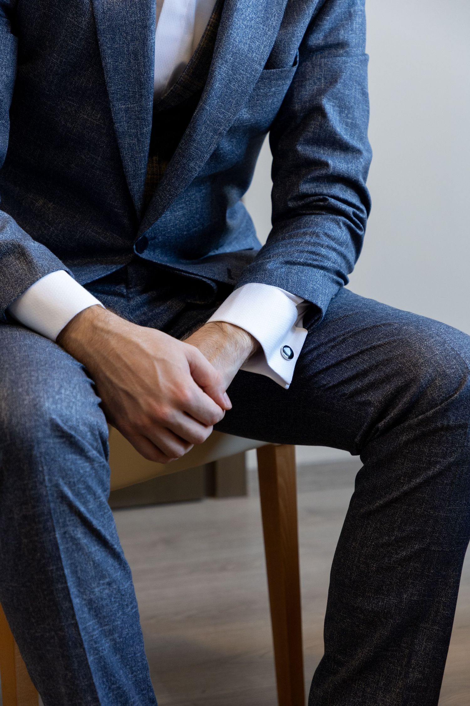 Close-up of groom adjusting cufflinks on navy blue suit sleeve.