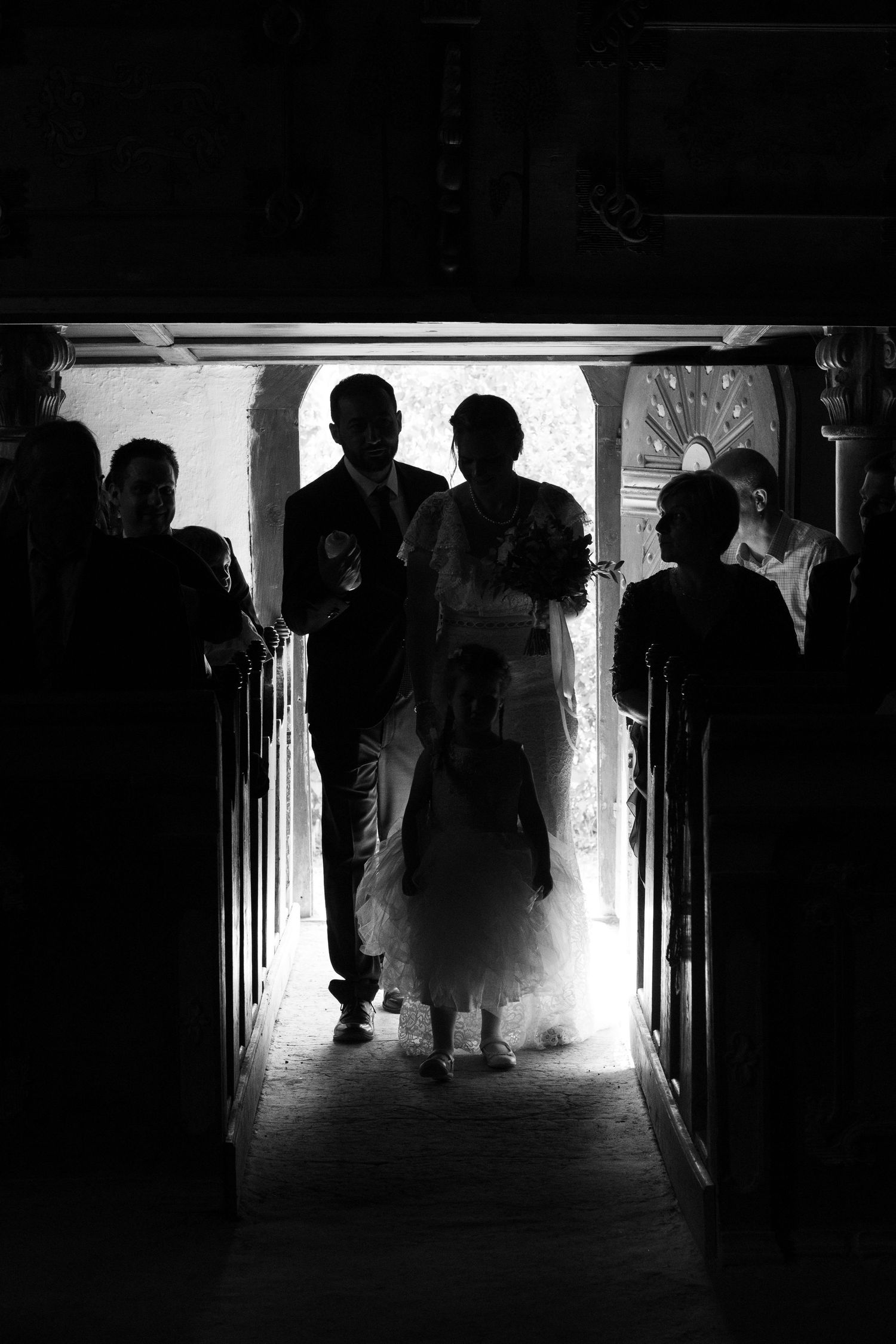 Dramatic silhouette of wedding party walking through church doorway backlit by bright sunlight.