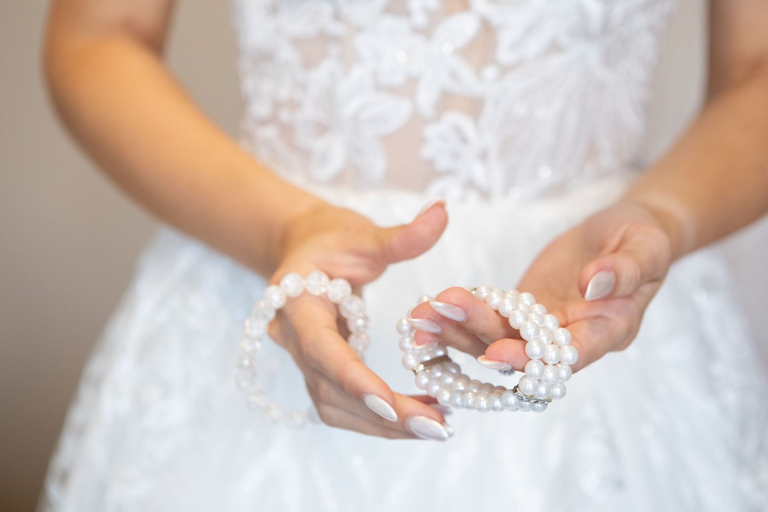 Delicate pearl accessories held in bride's hands against white wedding dress.