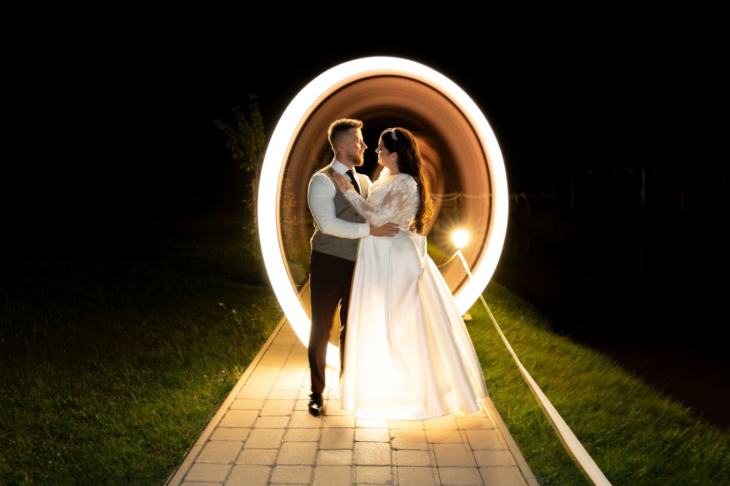 Newlyweds pose in illuminated circular archway during nighttime wedding photography.
