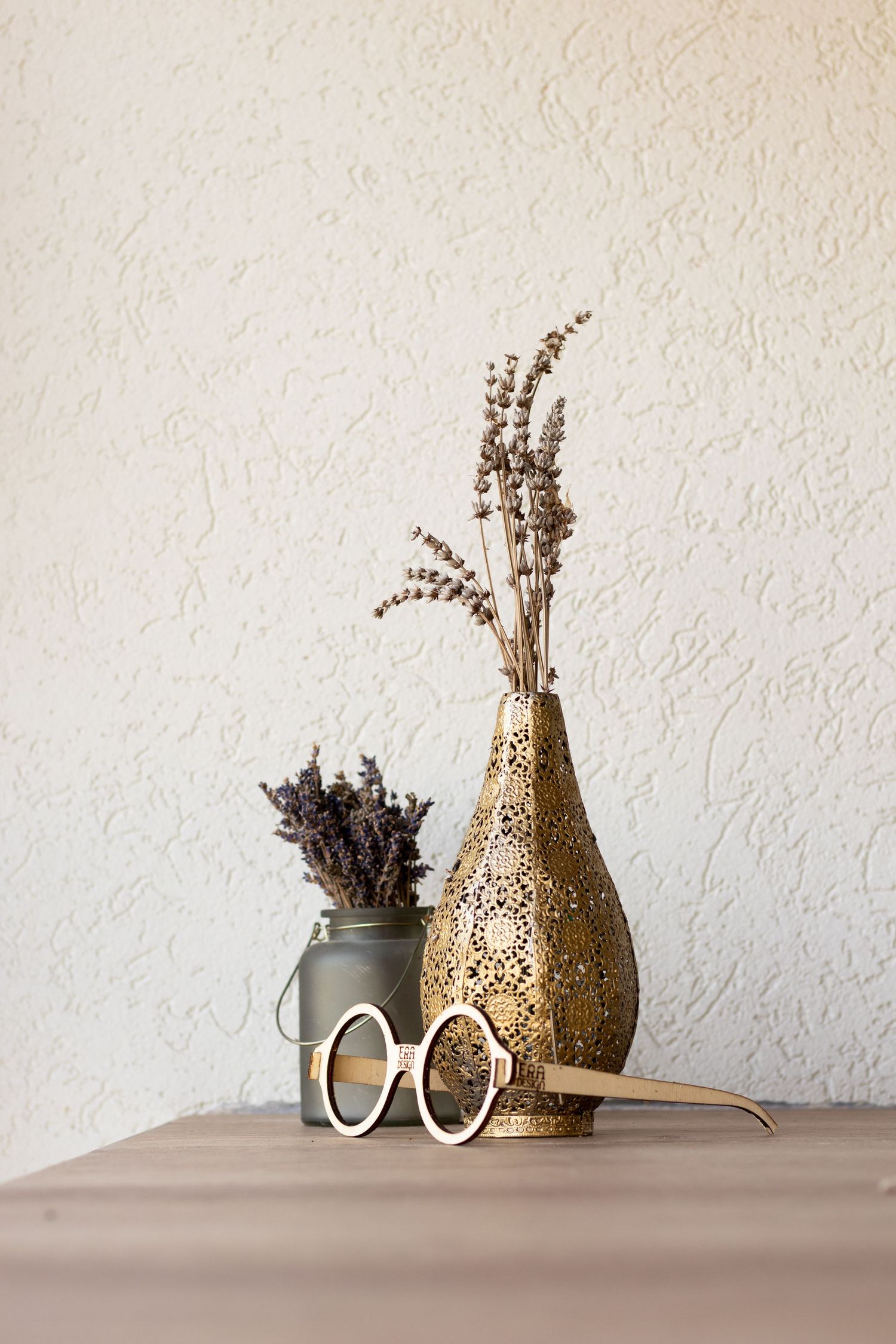Decorative vases and dried flowers arranged on table against textured wall.