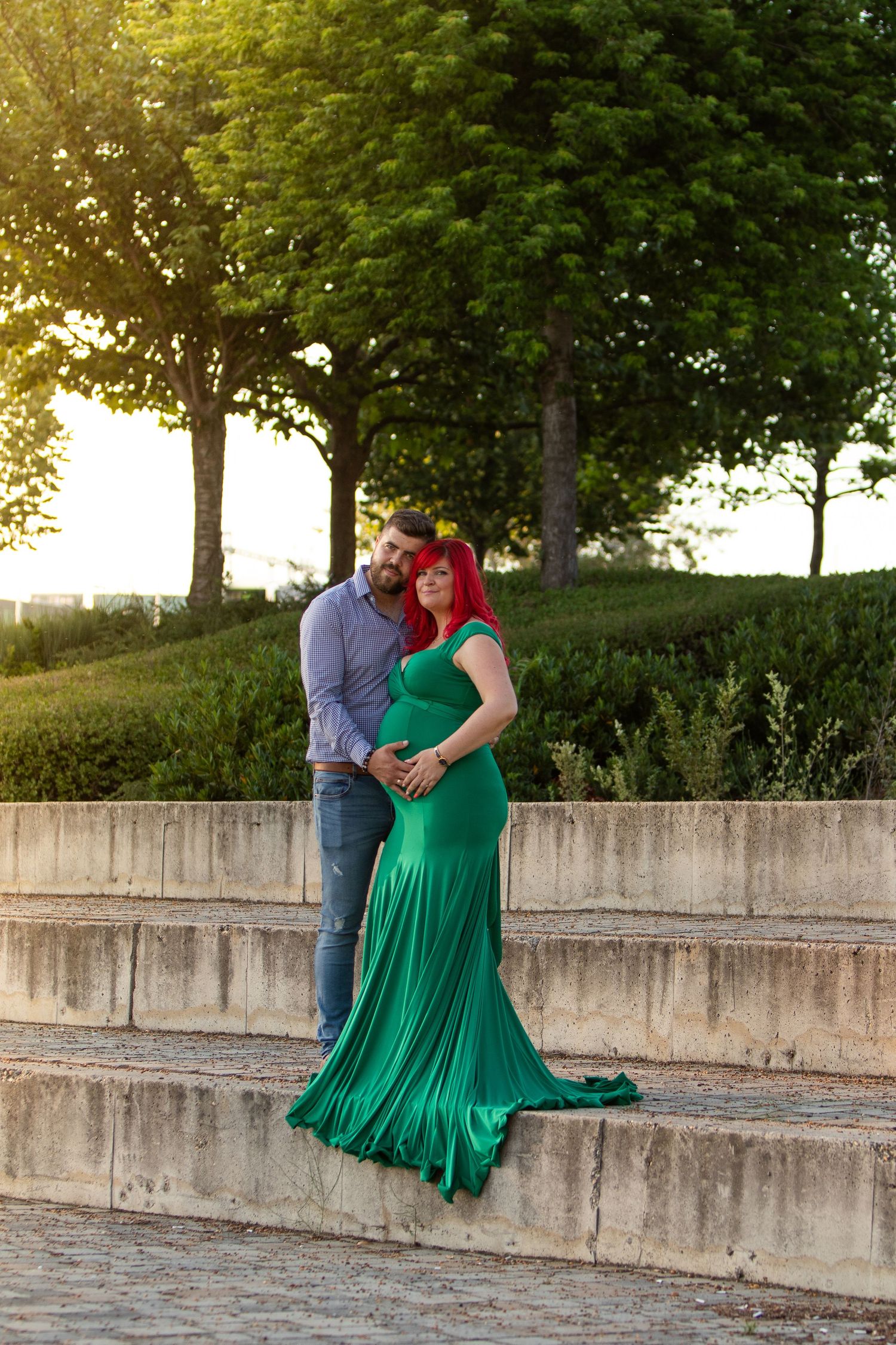 Couple poses on concrete wall during outdoor maternity photo session at sunset.