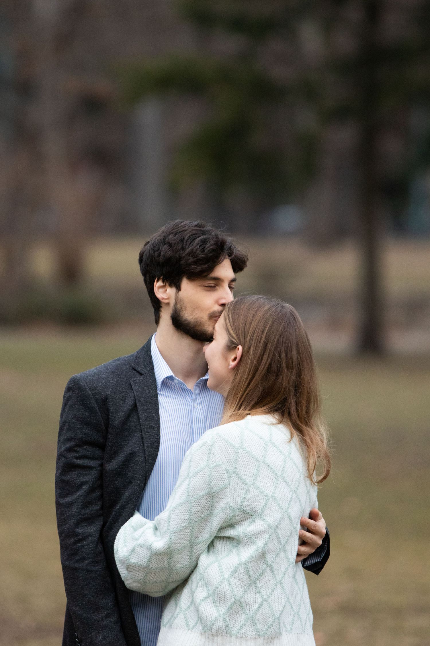 A romantic couple sharing an intimate moment outdoors in a park setting.