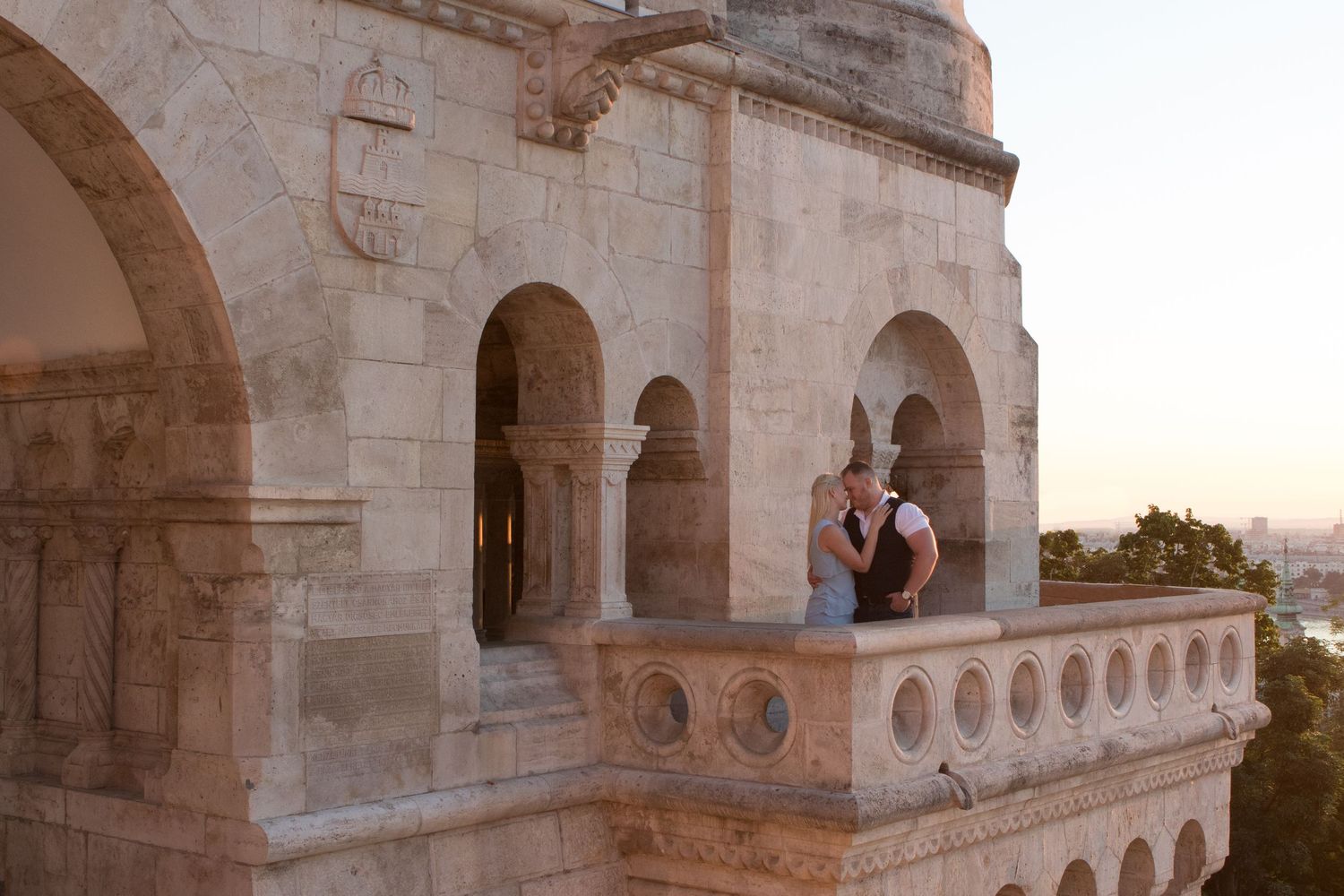 Couple standing together on ornate stone architecture balcony during sunset.