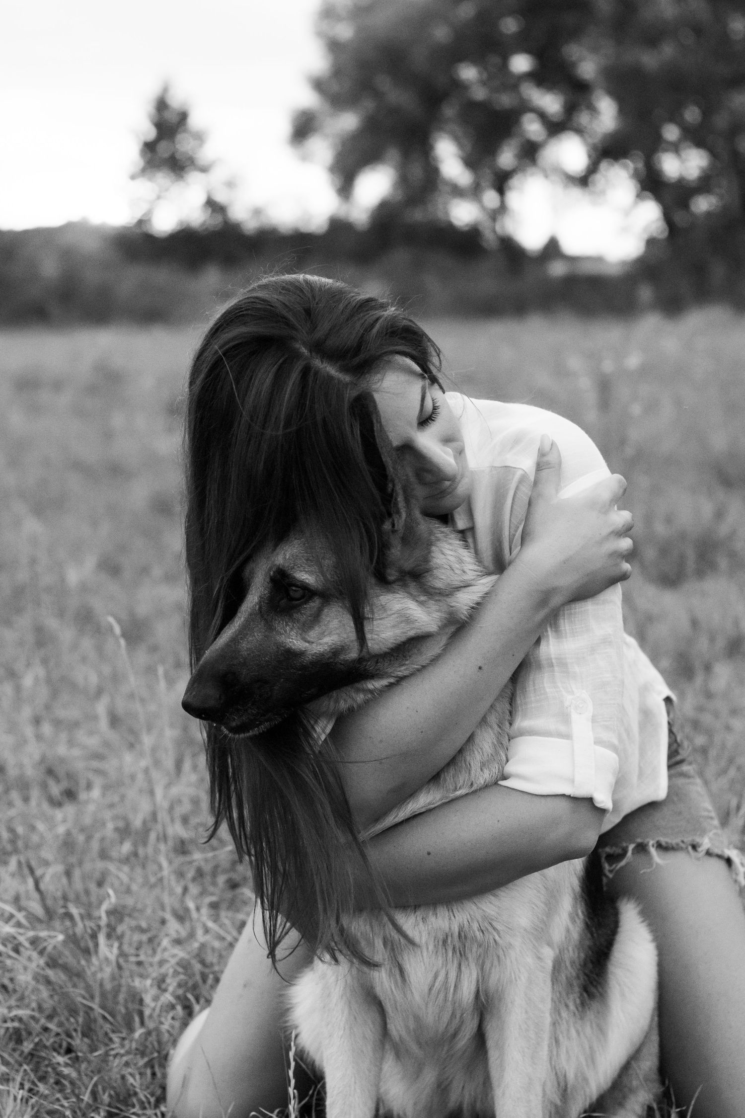 Black and white photo of a person cuddling with their German Shepherd mix dog in tall grass.