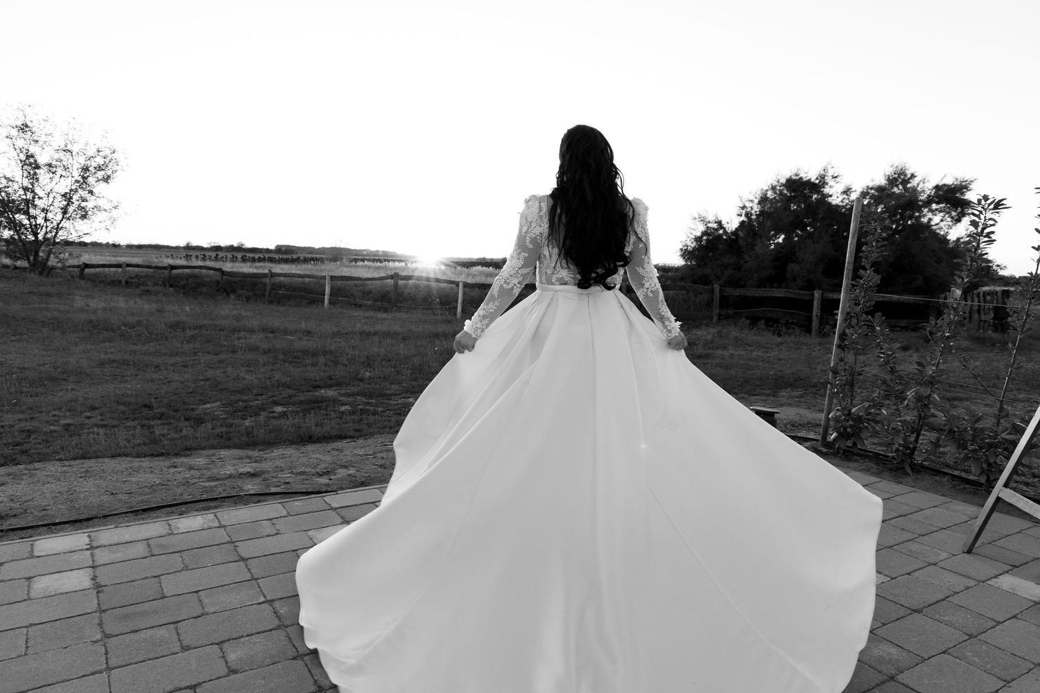Dramatic silhouette of a flowing wedding dress against a sunset landscape.