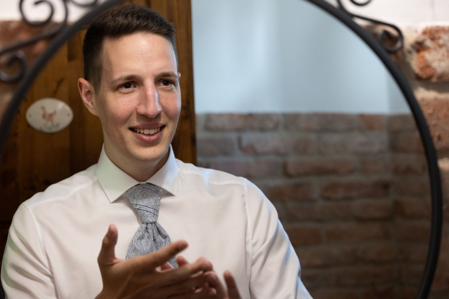 Candid portrait of a wedding guest in formal attire against a rustic brick wall background.