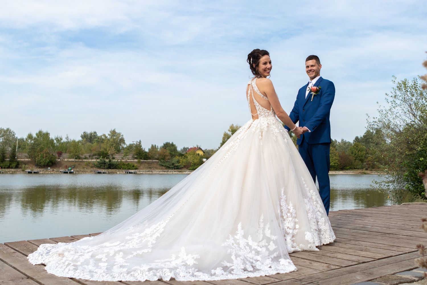 A wedding couple poses on a dock, showcasing a dramatic lace train against a lakeside backdrop.