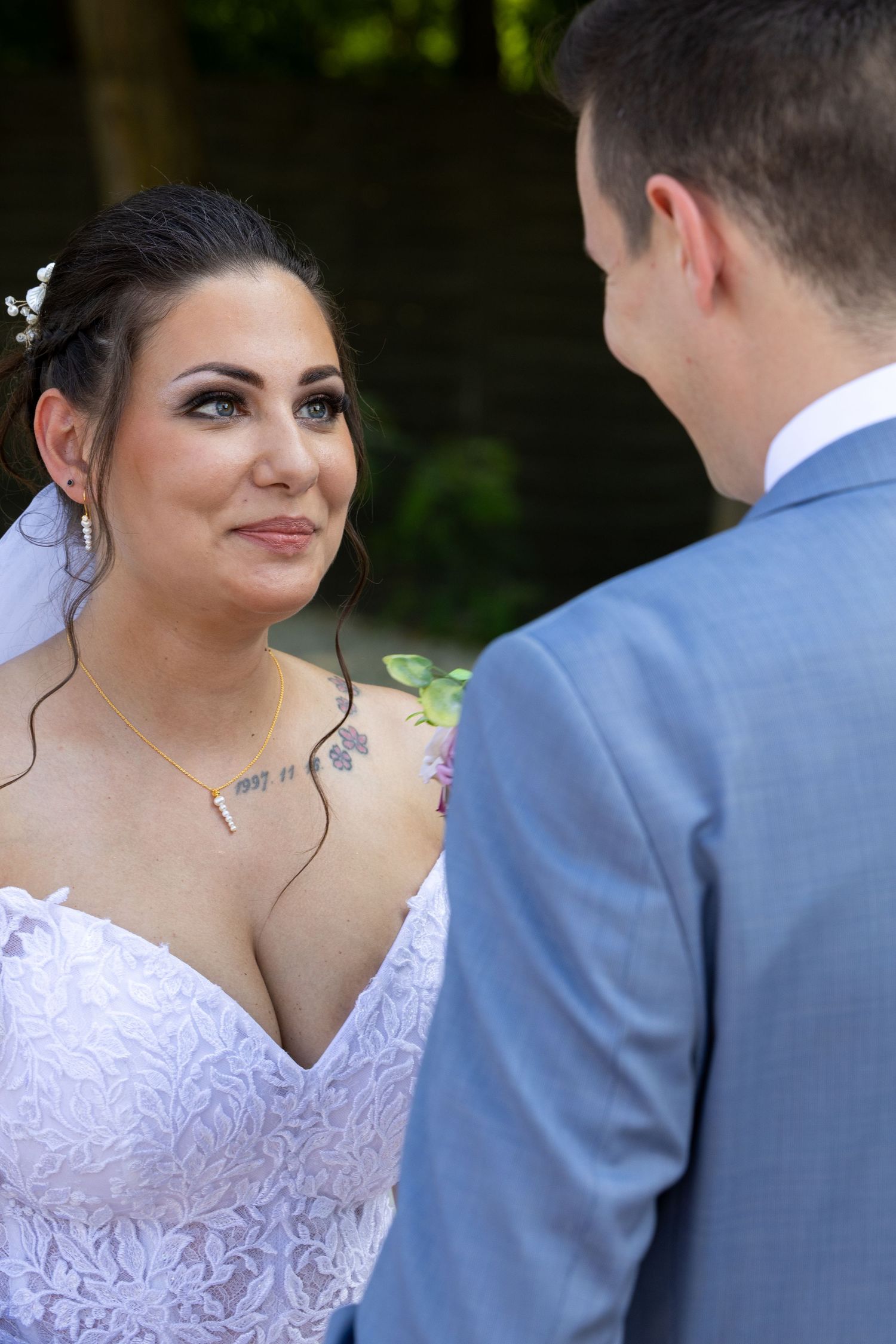 A close-up wedding photo showing a white lace dress and light blue suit during an outdoor ceremony.