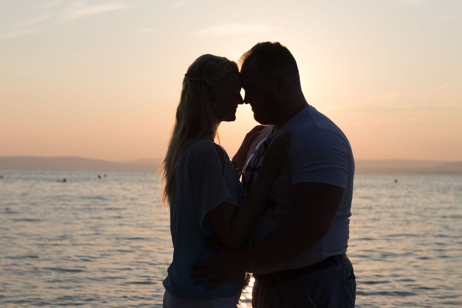 Romantic silhouettes against a golden sunset over calm waters.