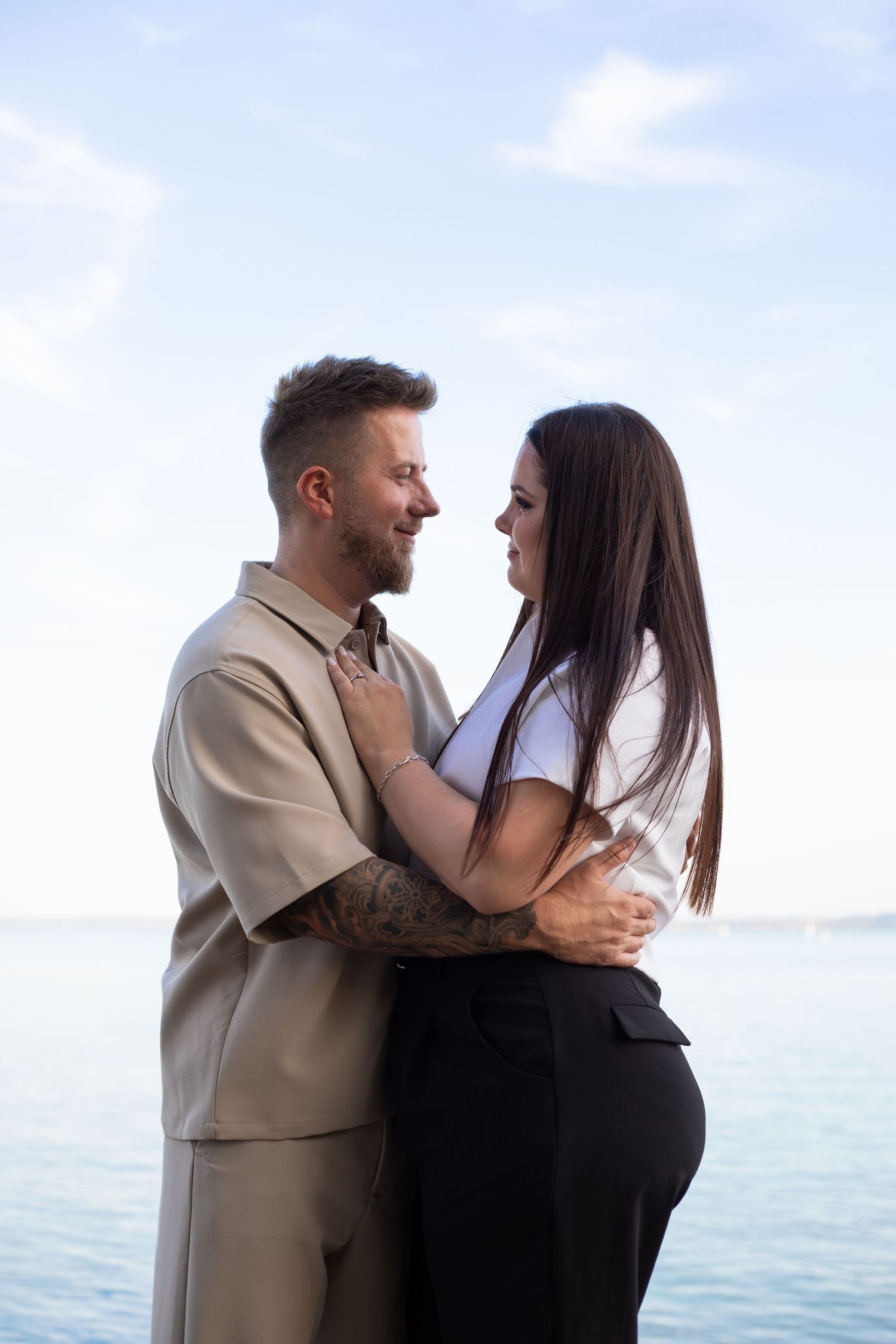 Romantic couple embracing and gazing at each other by the ocean on a clear day.
