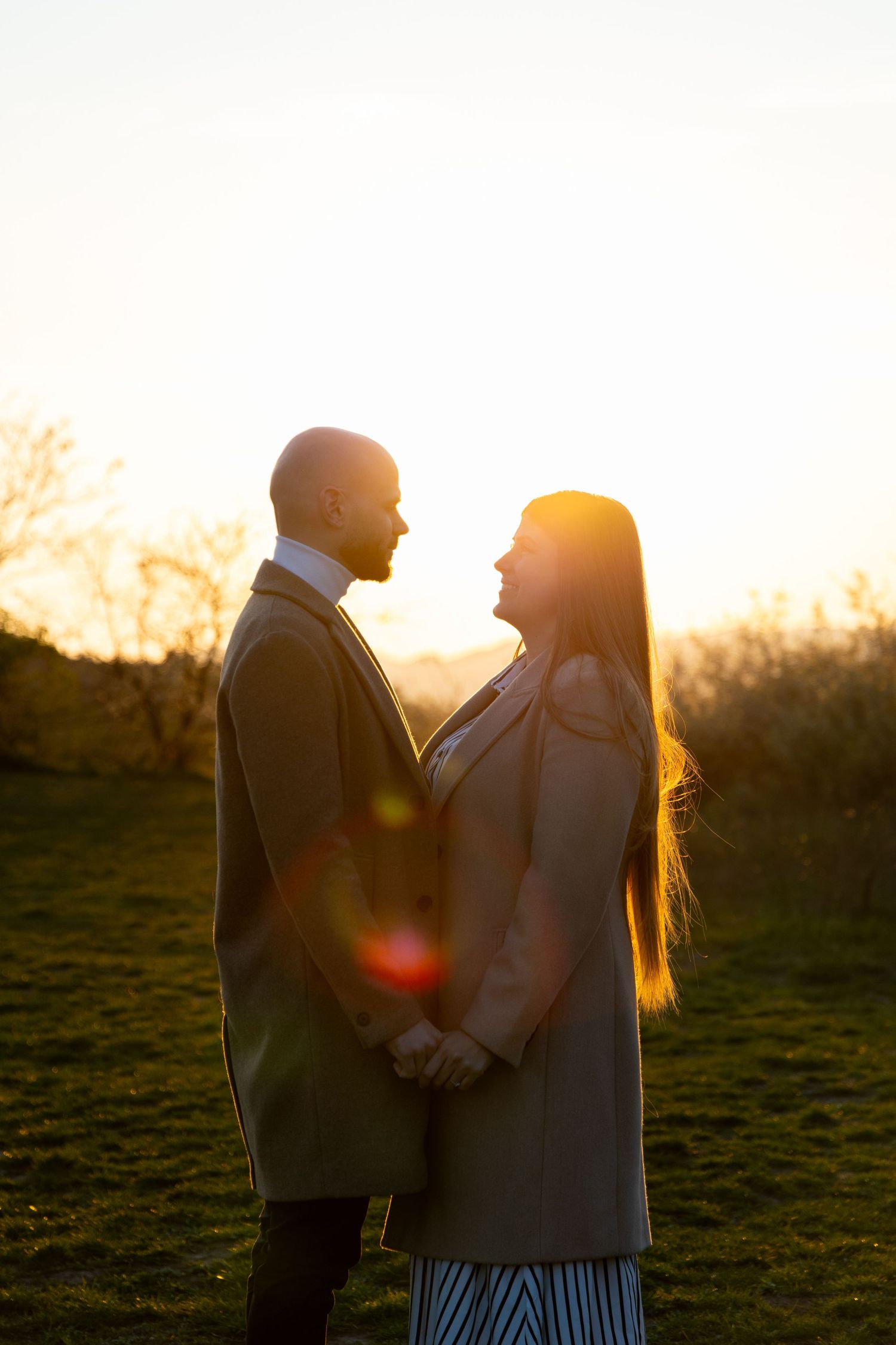 Couple holding hands facing each other in golden sunset backlight outdoors.