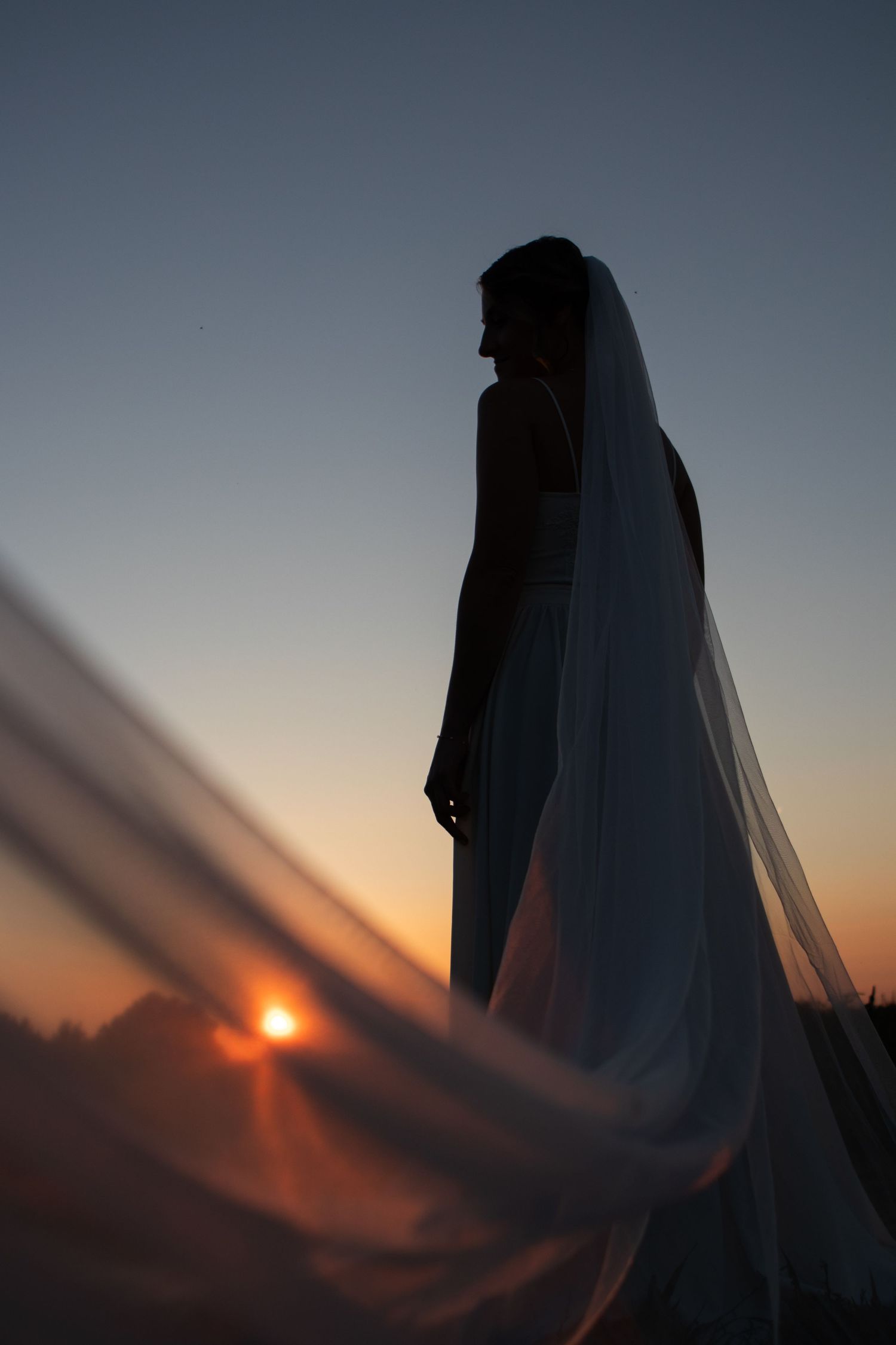 Ethereal wedding veil flowing in the wind against a sunset sky.