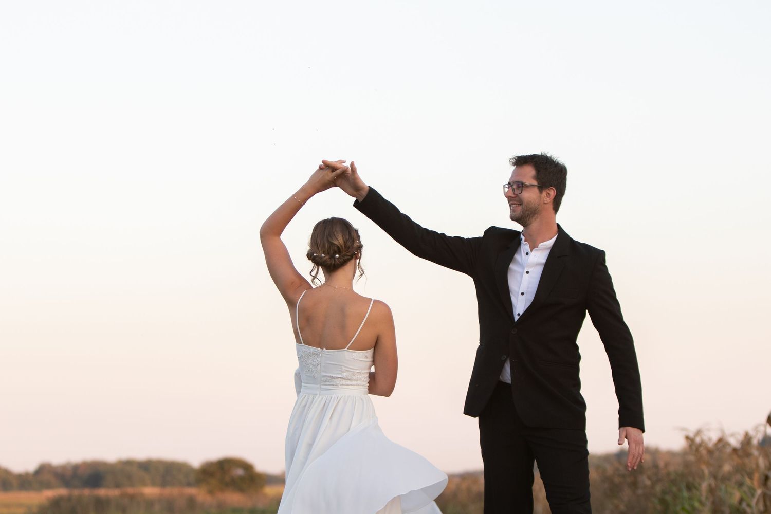 Wedding couple twirling and dancing in a field at sunset.