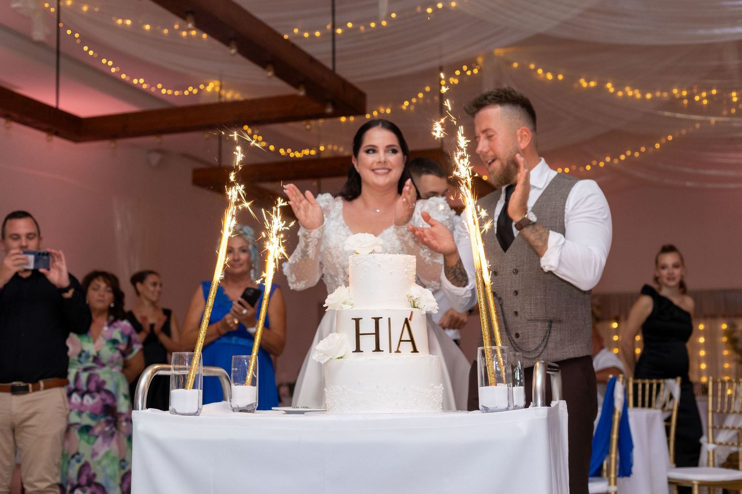 Newlyweds toast at their reception table decorated with lights and 'HIA' signage.