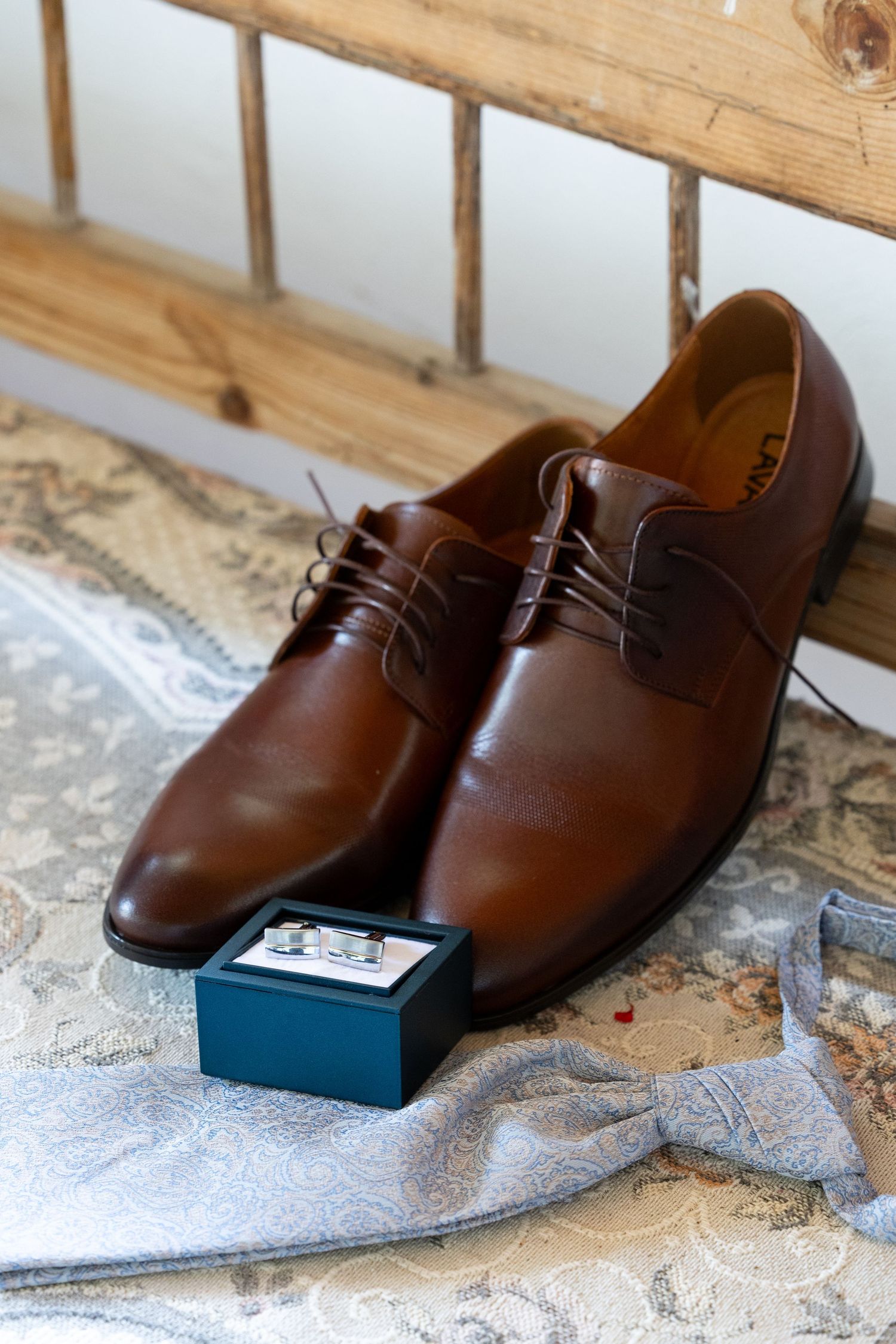 Brown leather dress shoes and small box displayed on wooden bench for wedding day preparations.