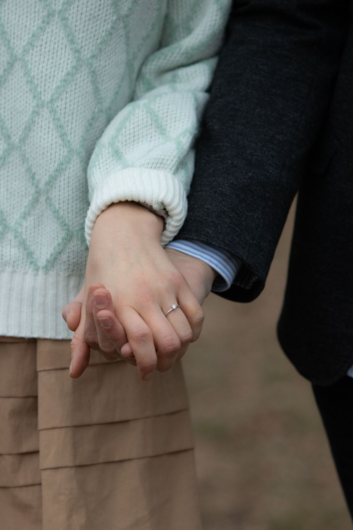 Close-up of two hands clasped together, with one person wearing a white sweater and the other wearing black.