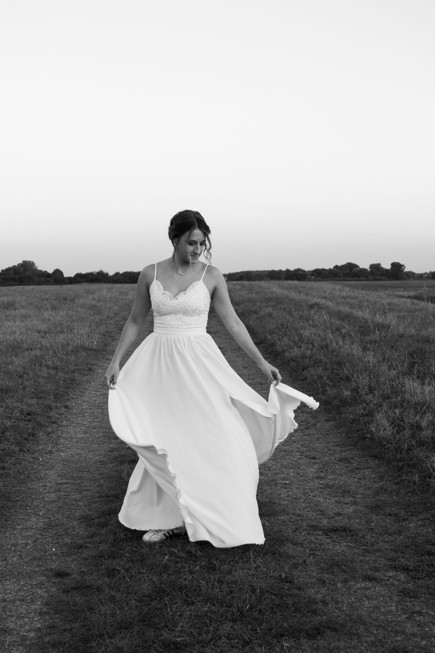 Black and white image of a bride in flowing white dress twirling in a field.
