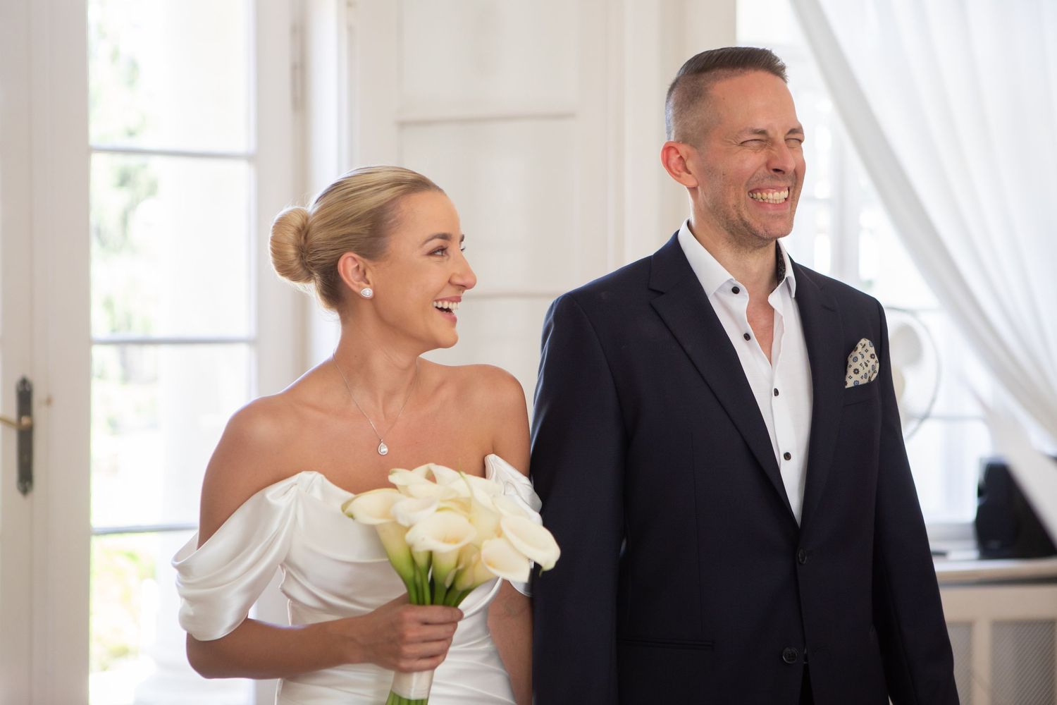 Wedding party members sharing joyful moments in an elegant white interior setting.