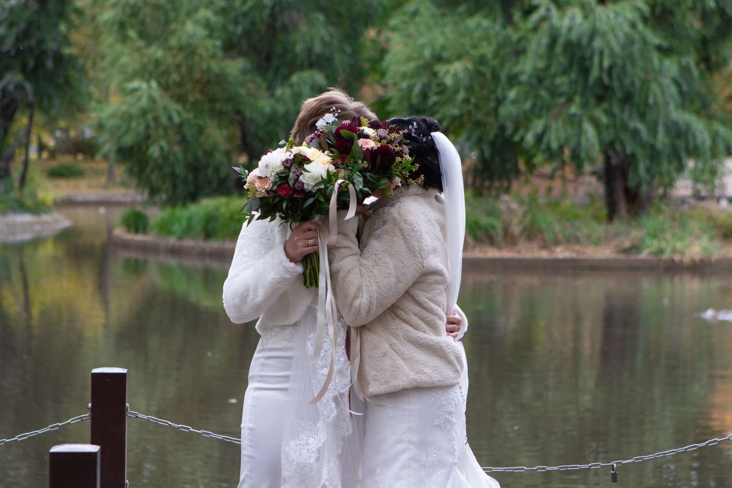 Wedding couple posing with bouquet by lakeside in natural setting.
