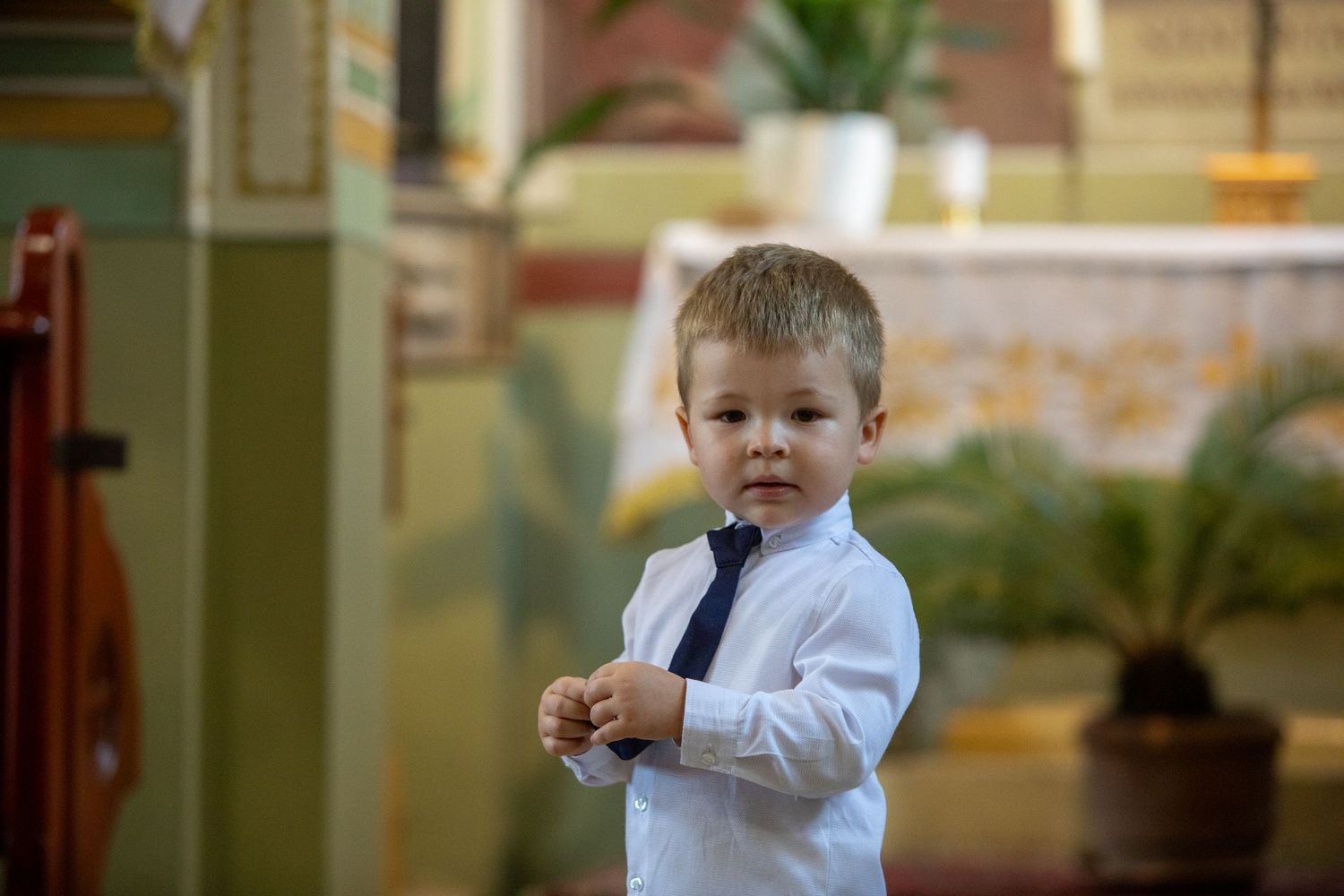 Young ring bearer in white shirt smiling during wedding ceremony.