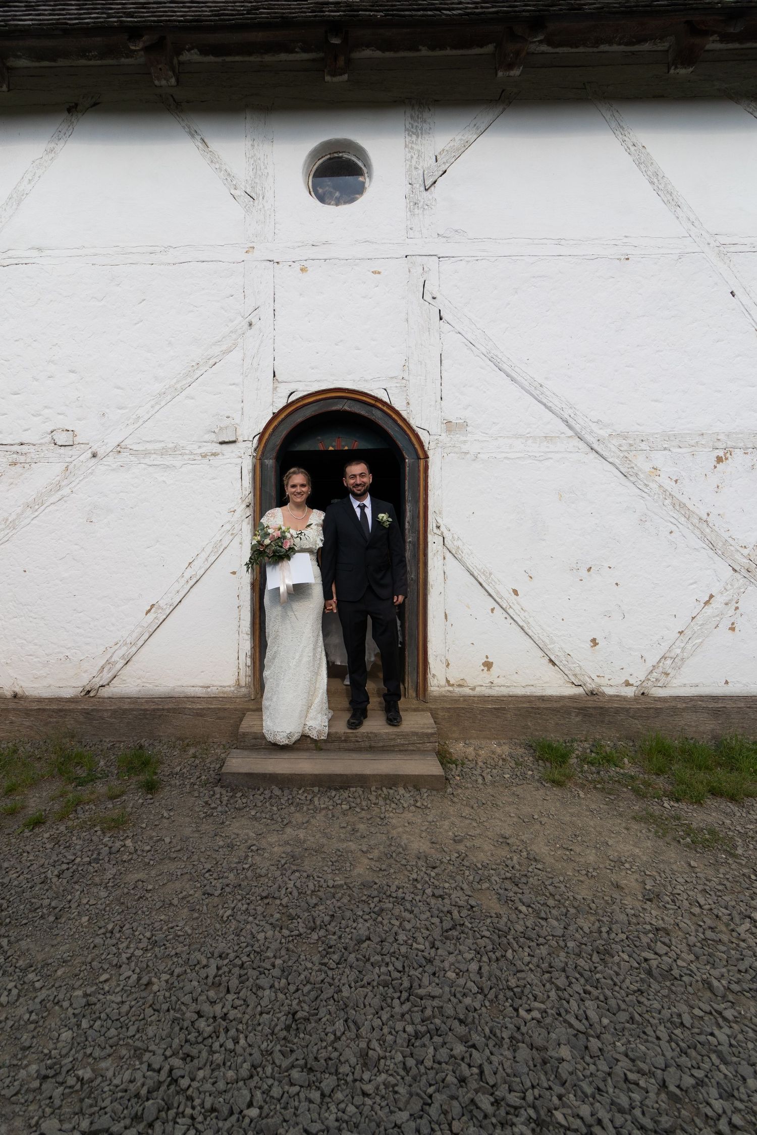 Rustic white building entrance with geometric patterns frames wedding couple.