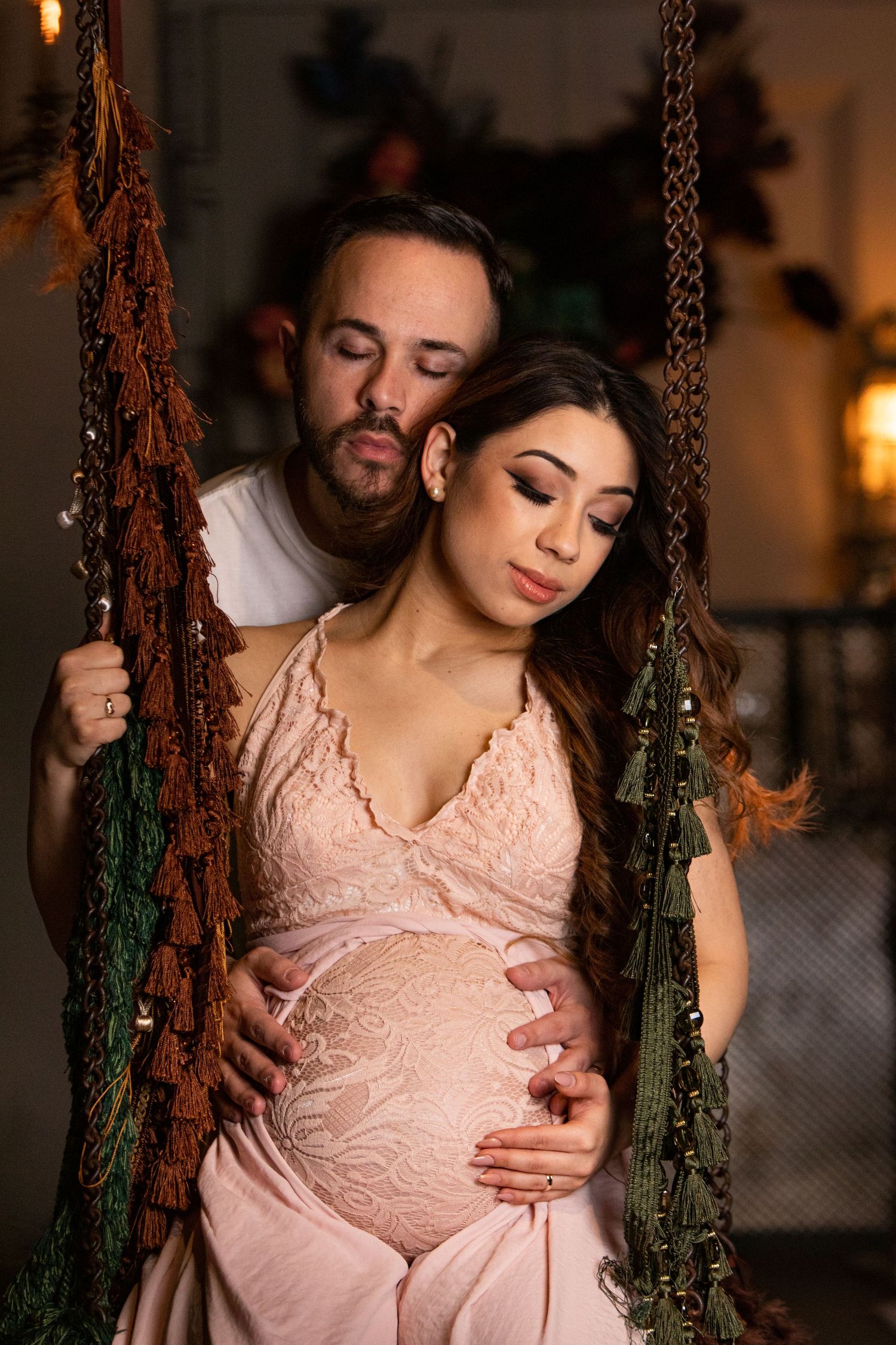 Romantic maternity photos on vintage swing decorated with greenery and soft lighting.