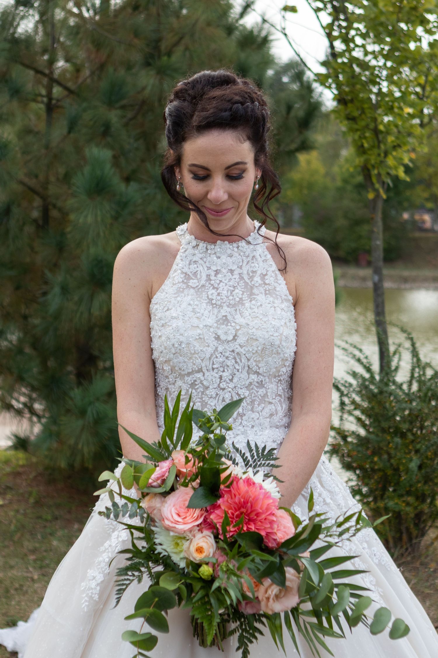 An elegant bridal portrait showcases a detailed lace halter dress and vibrant coral and pink bouquet.