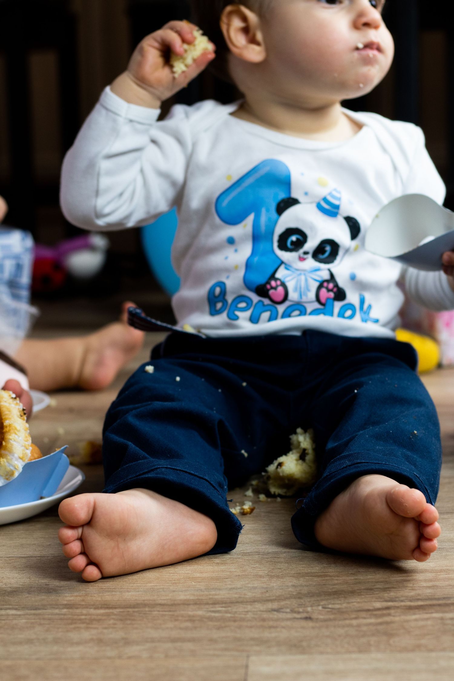 Close-up of small feet and panda-themed outfit while sitting on wooden floor.