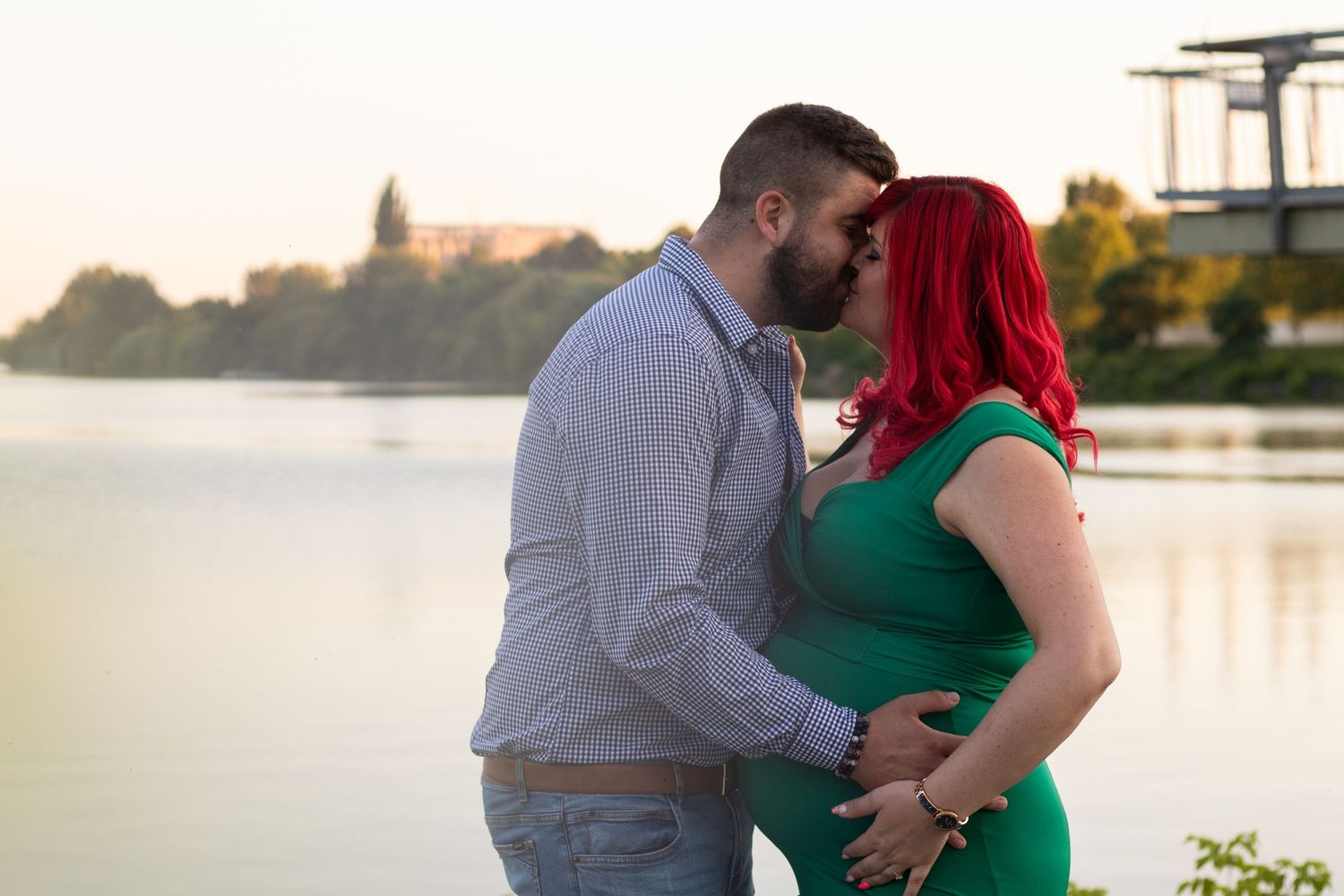 Sunset photoshoot by the water with couple in green dress and blue shirt.