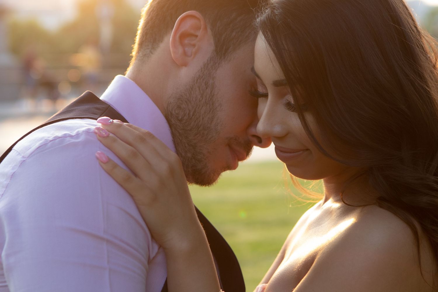 Romantic couple sharing an intimate moment in golden sunlight on a grassy field.